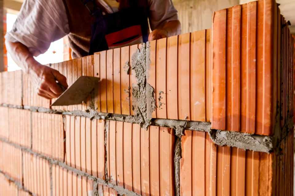 Ouvrier maçon appliquant du mortier sur un mur de briques en construction