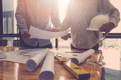 Deux professionnels du bâtiment examinent des plans architecturaux dans un bureau ensoleillé
