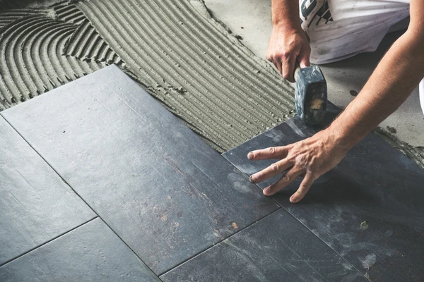 Chantier de pose de carrelage en extérieur, ouvrier agenouillé installant des dalles céramiques sur chape cimentée avec joints de dilatation