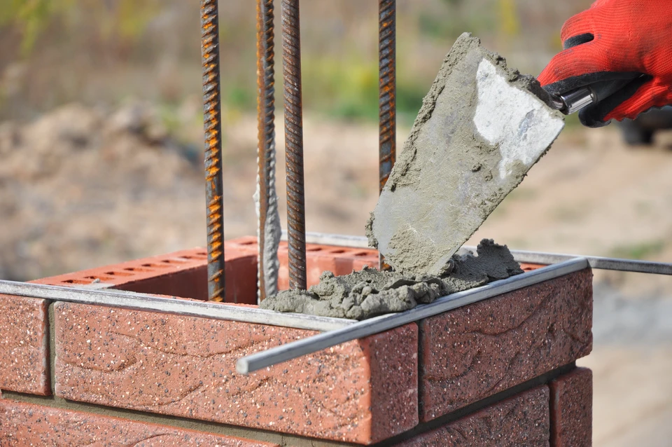 Ouvrier en bâtiment utilisant un niveau à bulle jaune pour vérifier l'alignement horizontal d'un mur en briques blanches en construction