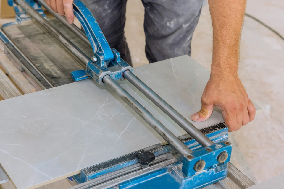 Ouvrier en équipement de sécurité coupe des carreaux de céramique avec une carrelette manuelle dans un bâtiment en construction